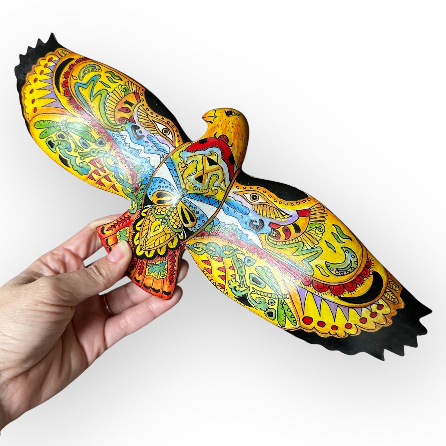 Colorful wooden bird sculpture held by a hand on a white background